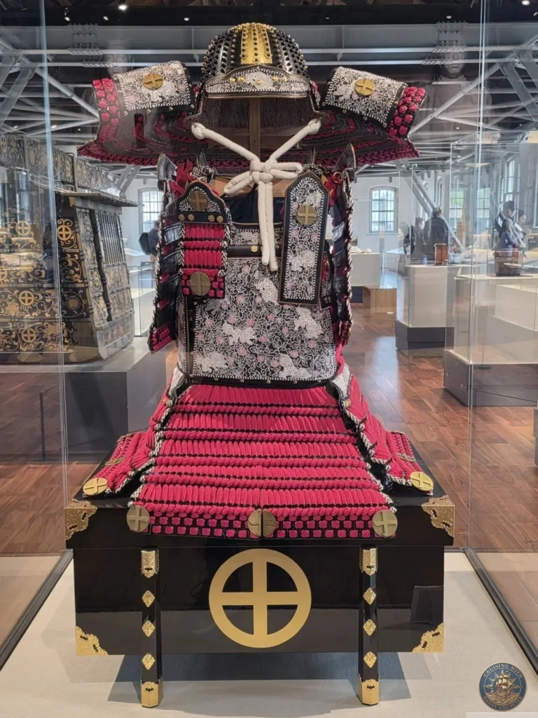 Ornate traditional samurai armor with black lacquer, vibrant red lacing, and gold accents displayed in a glass case at the Shoko Shuseikan UNESCO World Cultural Heritage Museum in Sengan-en, Kagoshima, Japan. Kagoshima Cruise Port Guide | Things to do in Kagoshima from cruise ship | One day in Kagoshima Japan itinerary by Danny and Peter.