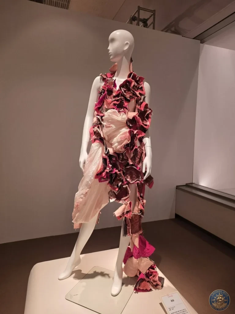 Dramatic pink and burgundy avant-garde dress with layered ruffles on mannequin at Fukuoka City Museum, Japan. Contemporary fashion art. Fukuoka Cruise Port Guide | Things to do in Fukuoka from cruise ship | One day in Fukuoka Japan itinerary by Danny and Peter.