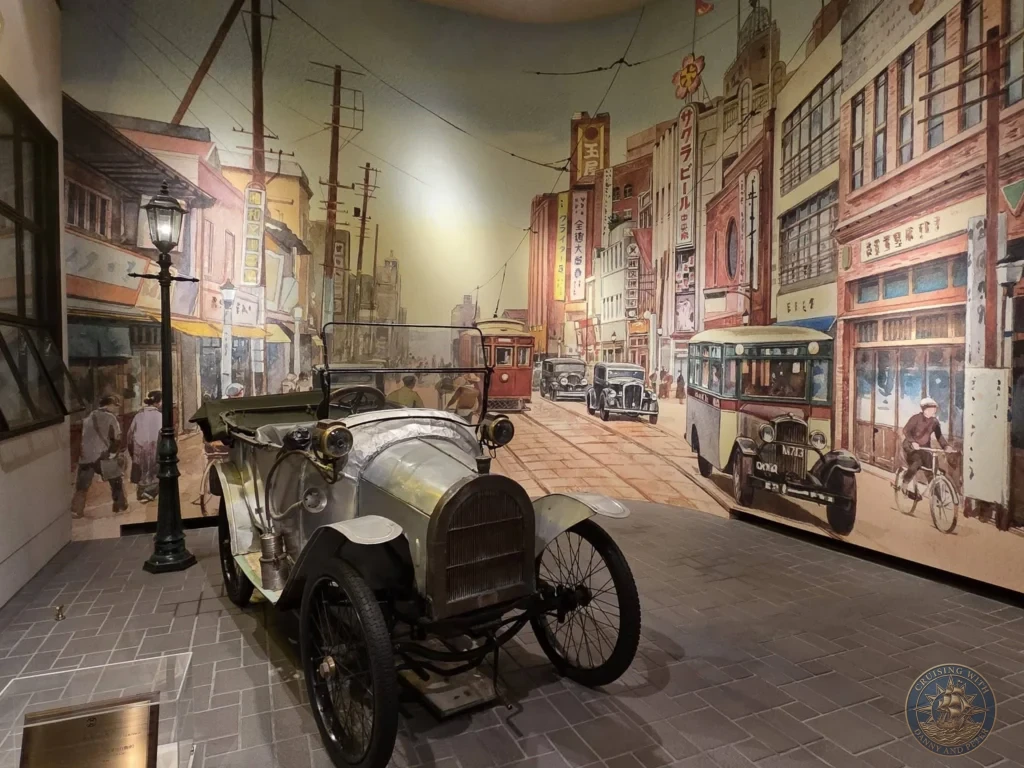 Vintage automobile with detailed historic street mural backdrop at Fukuoka City Museum, Japan. Transportation display. Fukuoka Cruise Port Guide | Things to do in Fukuoka from cruise ship | One day in Fukuoka Japan itinerary by Danny and Peter.