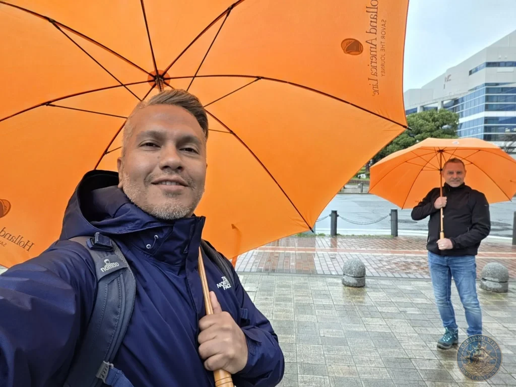 Danny and Peter posing with bright orange Holland America Line umbrellas in Fukuoka, Japan. Cruise port scene. Fukuoka Cruise Port Guide | Things to do in Fukuoka from cruise ship | One day in Fukuoka Japan itinerary by Danny and Peter.