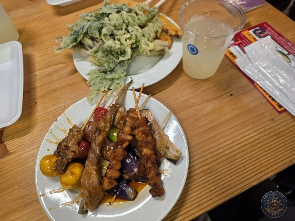 Plates of grilled kushiyaki skewers and crispy vegetable tempura with drinks at Hirome Market in Kochi, Japan. Popular local street food. Kochi Cruise Port Guide | Things to do in Kochi from cruise ship | One day in Kochi Japan itinerary by Danny and Peter.