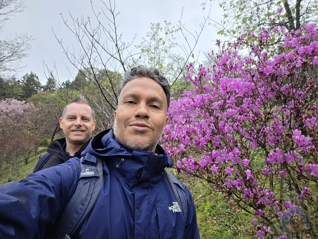 Danny and Peter taking a selfie in front of blooming pink azaleas at Makino Botanical Garden in Kochi, Japan. Spring garden flowers. Kochi Cruise Port Guide | Things to do in Kochi from cruise ship | One day in Kochi Japan itinerary by Danny and Peter.