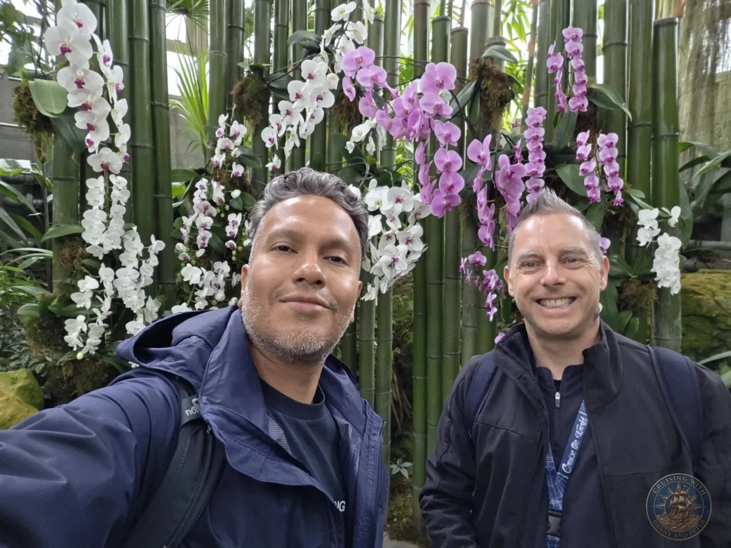 Danny and Peter taking a selfie with white and purple orchids against bamboo at Makino Botanical Garden in Kochi, Japan. Tropical greenhouse scene. Kochi Cruise Port Guide | Things to do in Kochi from cruise ship | One day in Kochi Japan itinerary by Danny and Peter.