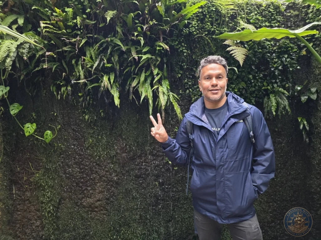 Danny making peace sign in front of lush moss and fern-covered wall at Makino Botanical Garden in Kochi, Japan. Tropical garden feature. Kochi Cruise Port Guide | Things to do in Kochi from cruise ship | One day in Kochi Japan itinerary by Danny and Peter.