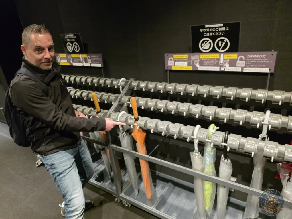 Peter pointing at umbrella rental lockers at teamLab Forest in Fukuoka, Japan. Practical visitor facility. Fukuoka Cruise Port Guide | Things to do in Fukuoka from cruise ship | One day in Fukuoka Japan itinerary by Danny and Peter.