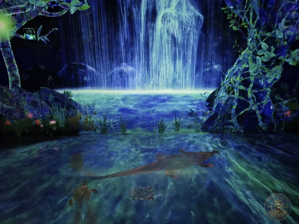 Dramatic glowing waterfall with dinosaurs and creatures in the immersive digital forest at teamLab Forest Fukuoka, Japan. teamLab art experience. Fukuoka Cruise Port Guide | Things to do in Fukuoka from cruise ship | One day in Fukuoka Japan itinerary by Danny and Peter.