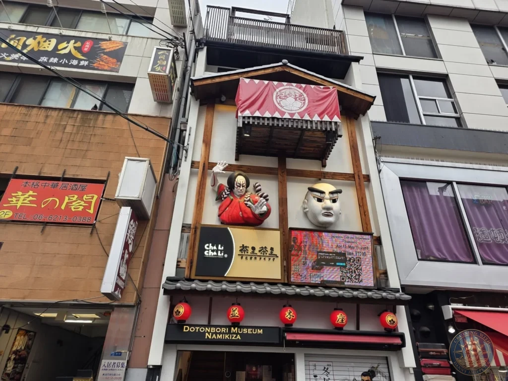 Kobe Japan Cruise Port Guide 2026 – Insider Tips & One Day Itinerary 95 Exterior of Dotonbori Museum Namikiza featuring kabuki-style figures, red lanterns, and traditional architecture in Osaka, Japan. Vibrant street scene from Kobe port day. Kobe Japan Cruise Port Guide | DIY Kobe Cruise Port to City Center | Things to do in Kobe from cruise ship | Westerdam Kobe Docking Location | One day in Kobe Japan itinerary by Danny and Peter.