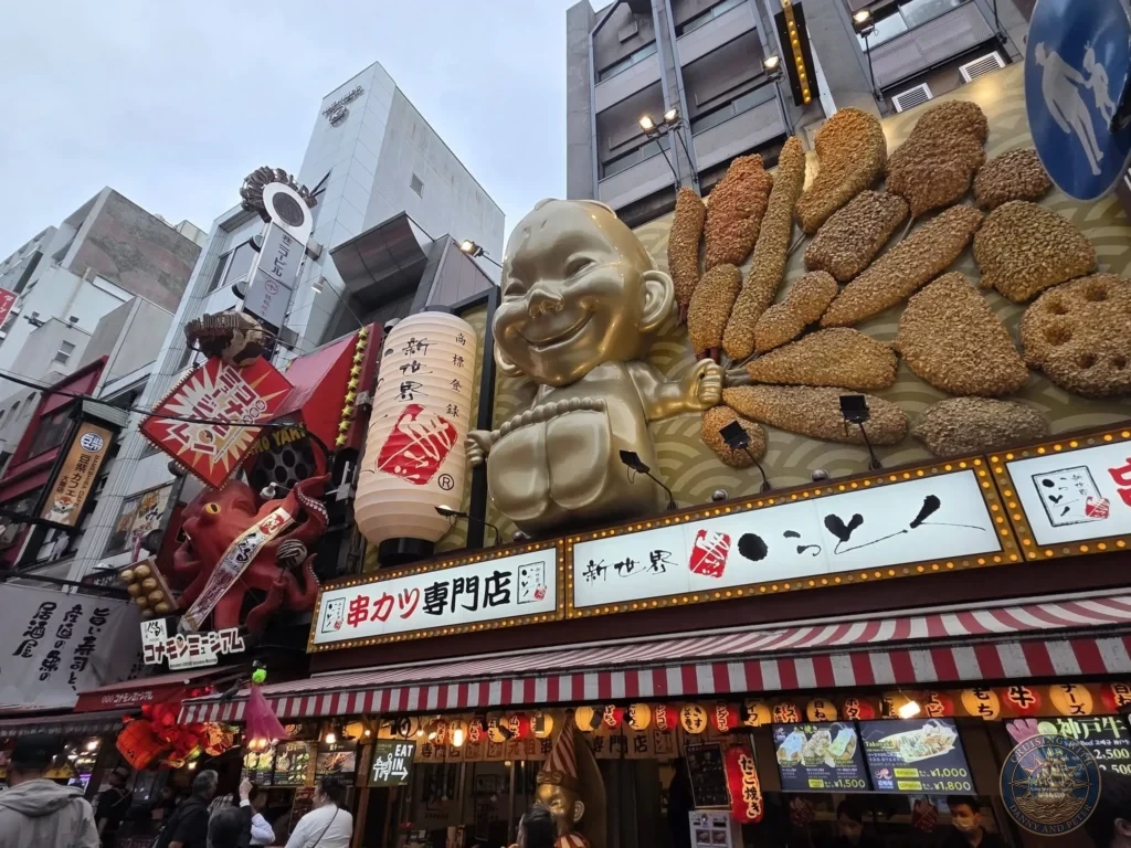 Kobe Japan Cruise Port Guide 2026 – Insider Tips & One Day Itinerary 24 Colorful Dotonbori street in Osaka featuring a large golden Billiken statue, kushikatsu displays, red octopus, and lanterns. Lively food street from Kobe port day. Kobe Japan Cruise Port Guide | DIY Kobe Cruise Port to City Center | Things to do in Kobe from cruise ship | Westerdam Kobe Docking Location | One day in Kobe Japan itinerary by Danny and Peter.