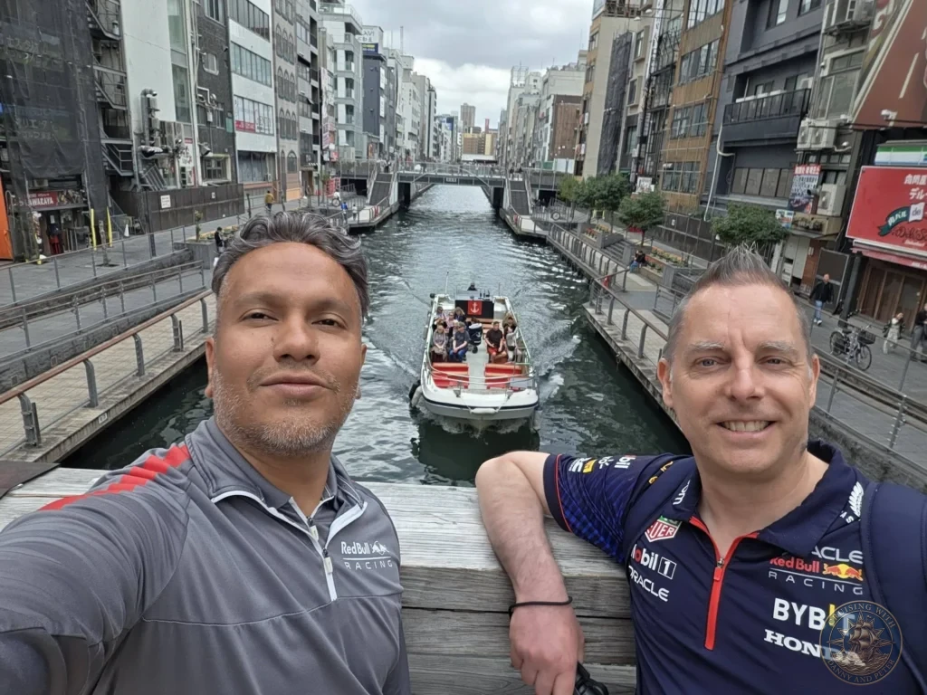 Kobe Japan Cruise Port Guide 2026 – Insider Tips & One Day Itinerary 34 Danny and Peter taking a selfie on a bridge overlooking the Dotonbori canal with a tourist boat passing below in Osaka, Japan. Canal view from Kobe port day. Kobe Japan Cruise Port Guide | DIY Kobe Cruise Port to City Center | Things to do in Kobe from cruise ship | Westerdam Kobe Docking Location | One day in Kobe Japan itinerary by Danny and Peter.