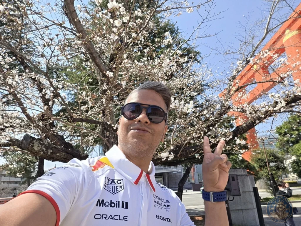 Kobe Japan Cruise Port Guide 2026 – Insider Tips & One Day Itinerary 9 Selfie of Danny in sunglasses and Red Bull shirt making a peace sign under cherry blossoms with the orange torii of Heian Shrine in Kyoto, Japan. Spring visit from Kobe. Kobe Japan Cruise Port Guide | DIY Kobe Cruise Port to City Center | Things to do in Kobe from cruise ship | Westerdam Kobe Docking Location | One day in Kobe Japan itinerary by Danny and Peter.