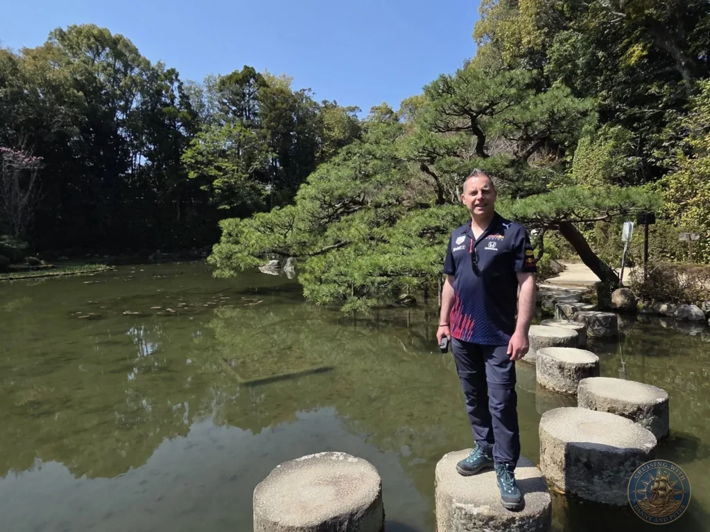 Kobe Japan Cruise Port Guide 2026 – Insider Tips & One Day Itinerary 57 Peter standing on stone stepping stones across a pond in the gardens of Heian Shrine under a clear blue sky in Kyoto, Japan. Shrine gardens from Kobe port day. Kobe Japan Cruise Port Guide | DIY Kobe Cruise Port to City Center | Things to do in Kobe from cruise ship | Westerdam Kobe Docking Location | One day in Kobe Japan itinerary by Danny and Peter.