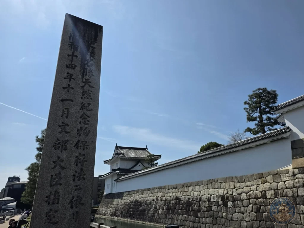 Kobe Japan Cruise Port Guide 2026 – Insider Tips & One Day Itinerary 77 Stone monument with Japanese inscriptions in front of the white walls and stone foundation of Nijo Castle under a blue sky in Kyoto, Japan. Historic castle grounds from Kobe port day. Kobe Japan Cruise Port Guide | DIY Kobe Cruise Port to City Center | Things to do in Kobe from cruise ship | Westerdam Kobe Docking Location | One day in Kobe Japan itinerary by Danny and Peter.