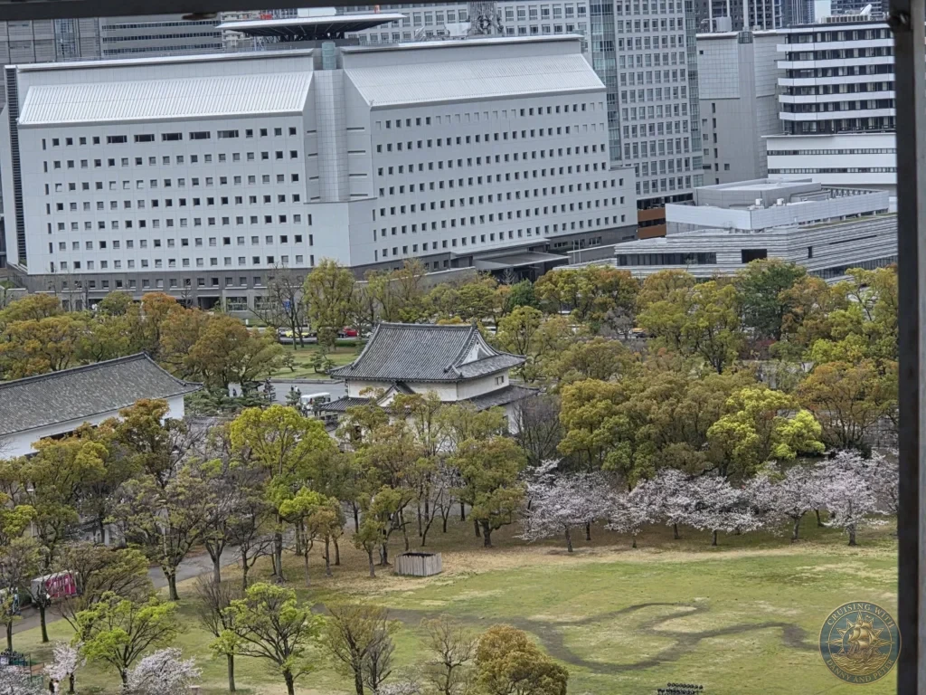 Kobe Japan Cruise Port Guide 2026 – Insider Tips & One Day Itinerary 106 Elevated view from Osaka Castle overlooking the castle grounds with traditional buildings, trees, cherry blossoms and modern city skyline in Osaka, Japan. Panoramic scene from Kobe port day. Kobe Japan Cruise Port Guide | DIY Kobe Cruise Port to City Center | Things to do in Kobe from cruise ship | Westerdam Kobe Docking Location | One day in Kobe Japan itinerary by Danny and Peter.