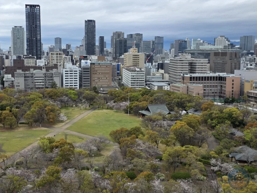 Kobe Japan Cruise Port Guide 2026 – Insider Tips & One Day Itinerary 108 Elevated view from Osaka Castle overlooking the park grounds and the modern Osaka city skyline under cloudy skies in Osaka, Japan. City panorama from Kobe port day. Kobe Japan Cruise Port Guide | DIY Kobe Cruise Port to City Center | Things to do in Kobe from cruise ship | Westerdam Kobe Docking Location | One day in Kobe Japan itinerary by Danny and Peter.