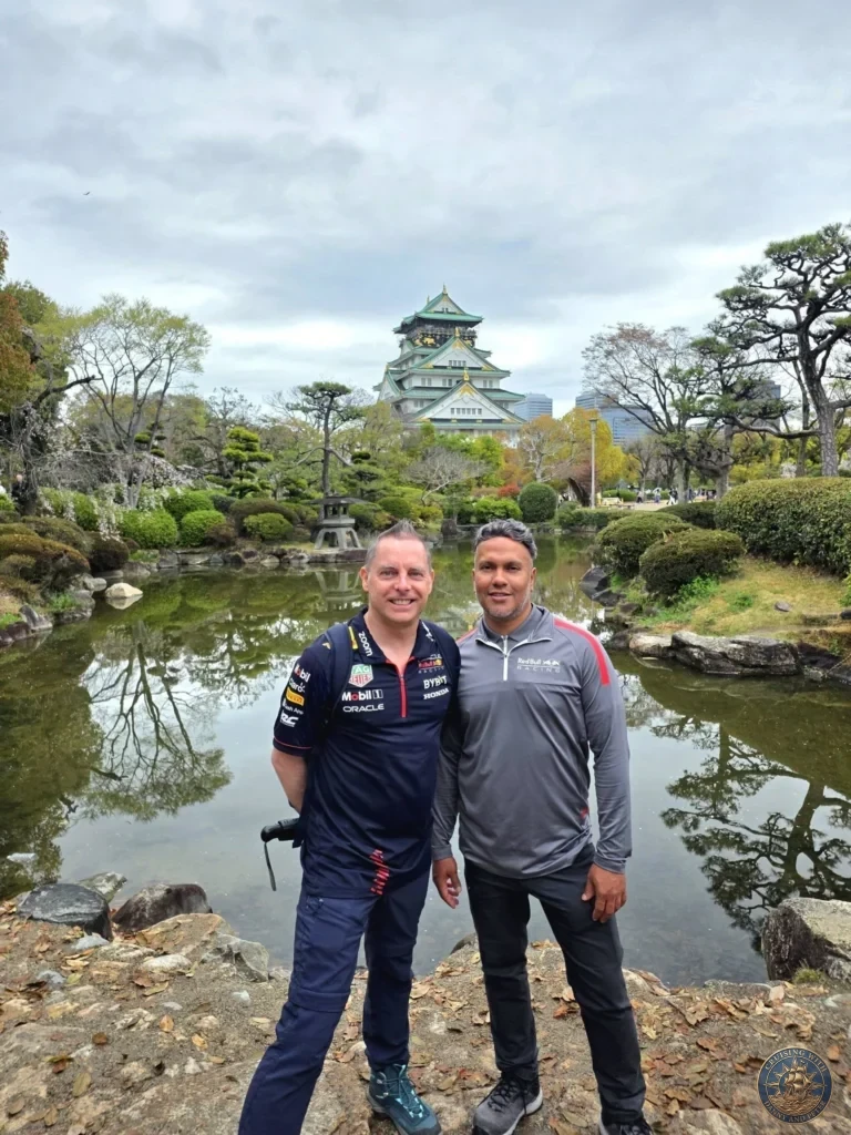Kobe Japan Cruise Port Guide 2026 – Insider Tips & One Day Itinerary 44 Danny and Peter standing together by a pond in the garden of Osaka Castle with the main keep visible in the background under cloudy skies in Osaka, Japan. Scenic garden moment from Kobe port day. Kobe Japan Cruise Port Guide | DIY Kobe Cruise Port to City Center | Things to do in Kobe from cruise ship | Westerdam Kobe Docking Location | One day in Kobe Japan itinerary by Danny and Peter.