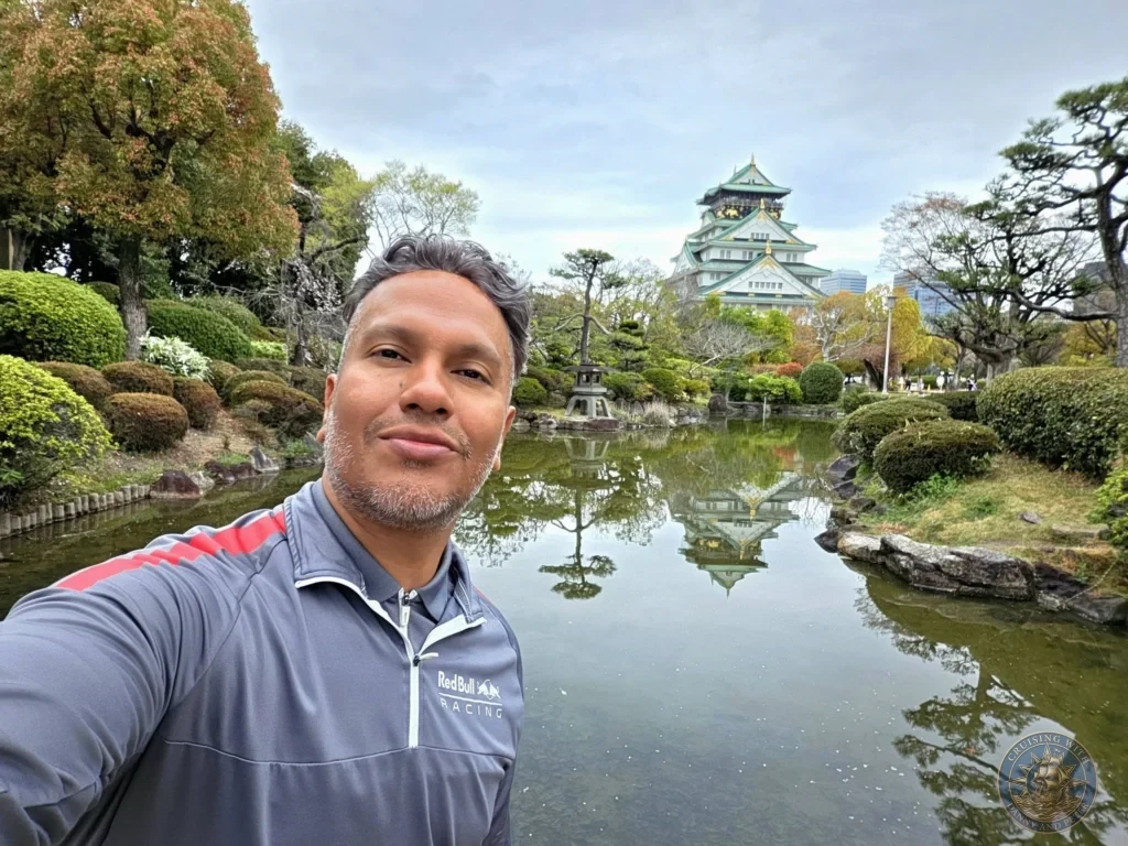 Kobe Japan Cruise Port Guide 2026 – Insider Tips & One Day Itinerary 17 Danny taking a selfie by the pond in Osaka Castle gardens with the main keep and its reflection visible in the background in Osaka, Japan. Peaceful garden moment from Kobe port day. Kobe Japan Cruise Port Guide | DIY Kobe Cruise Port to City Center | Things to do in Kobe from cruise ship | Westerdam Kobe Docking Location | One day in Kobe Japan itinerary by Danny and Peter.