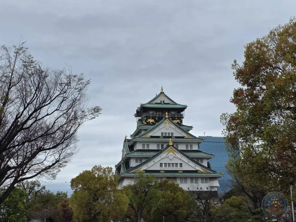 Kobe Japan Cruise Port Guide 2026 – Insider Tips & One Day Itinerary 25 The iconic main keep of Osaka Castle with its white walls, green roofs and golden accents rising above the trees under a cloudy sky in Osaka, Japan. Landmark view from Kobe port day. Kobe Japan Cruise Port Guide | DIY Kobe Cruise Port to City Center | Things to do in Kobe from cruise ship | Westerdam Kobe Docking Location | One day in Kobe Japan itinerary by Danny and Peter.