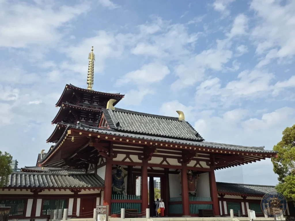 Kobe Japan Cruise Port Guide 2026 – Insider Tips & One Day Itinerary 7 The grand Niomon Gate of Shitennoji Temple featuring Nio guardian statues, with the golden spire of the five-story pagoda rising behind under a blue sky with scattered clouds; ideal for a Kobe Japan Cruise Port Guide, DIY Kobe Cruise Port to City Center, Things to do in Kobe from cruise ship, Westerdam Kobe Docking Location, or One day in Kobe Japan itinerary, by Danny and Peter.