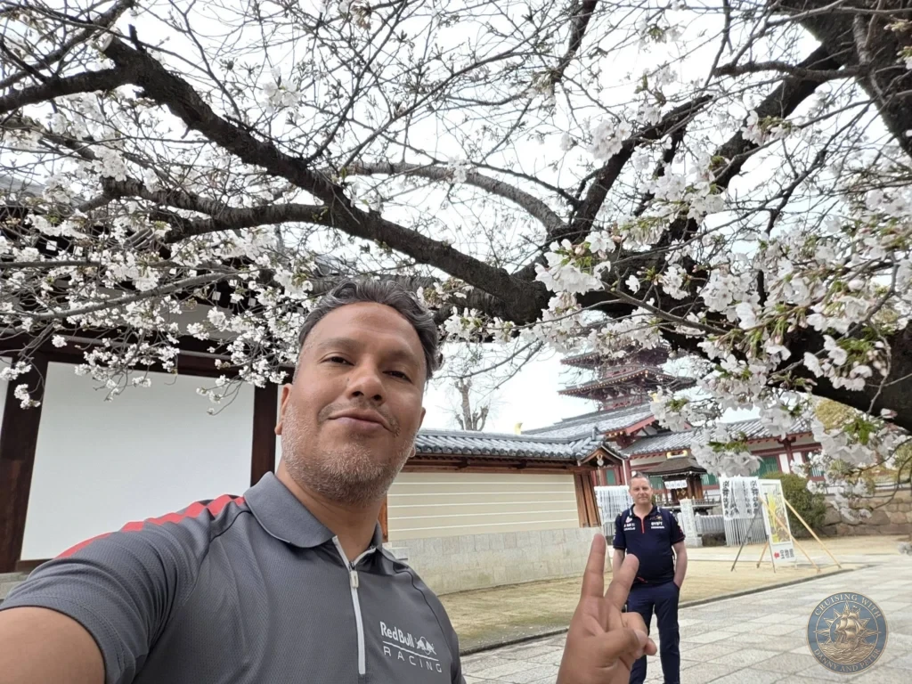 Kobe Japan Cruise Port Guide 2026 – Insider Tips & One Day Itinerary 139 Danny taking a selfie while making a peace sign, with Peter standing in the background under blooming cherry blossom tree branches at Shitennoji Temple in Osaka, Japan; ideal for a Kobe Japan Cruise Port Guide, DIY Kobe Cruise Port to City Center, Things to do in Kobe from cruise ship, MS Westerdam Kobe Docking Location, or One day in Kobe Japan itinerary, by Danny and Peter.