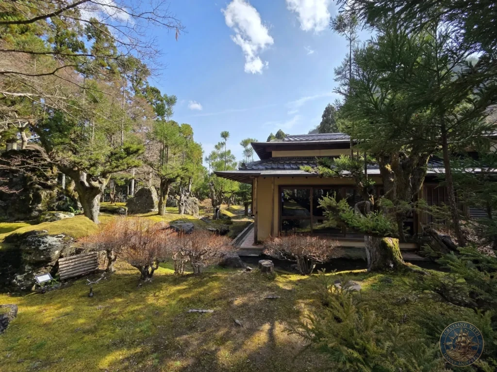 Kobe Japan Cruise Port Guide 2026 – Insider Tips & One Day Itinerary 78 Traditional Japanese building surrounded by mossy garden, rocks, and trees under a blue sky at Shozan Resort Garden in Kyoto, Japan. Beautiful garden stop from Kobe port day. Kobe Japan Cruise Port Guide | DIY Kobe Cruise Port to City Center | Things to do in Kobe from cruise ship | Westerdam Kobe Docking Location | One day in Kobe Japan itinerary by Danny and Peter.