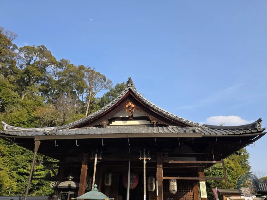 Kobe Japan Cruise Port Guide 2026 – Insider Tips & One Day Itinerary 94 Traditional Japanese shrine hall with curved tiled roof, lanterns, and hanging ropes under a clear blue sky at Shozan Resort Garden in Kyoto, Japan. Historic shrine architecture from Kobe port day. Kobe Japan Cruise Port Guide | DIY Kobe Cruise Port to City Center | Things to do in Kobe from cruise ship | Westerdam Kobe Docking Location | One day in Kobe Japan itinerary by Danny and Peter.