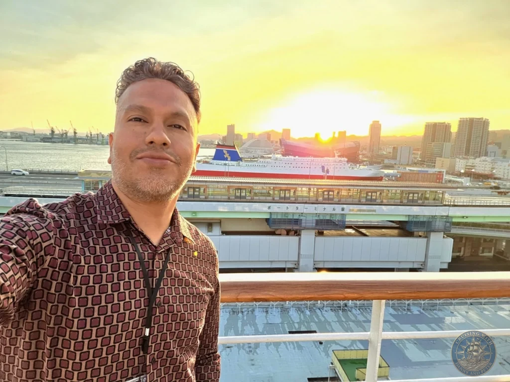 Kobe Japan Cruise Port Guide 2026 – Insider Tips & One Day Itinerary 20 Danny taking a solo selfie on the cruise ship deck with a bright golden sunset illuminating Kobe harbor, Port Terminal Station, and city buildings behind him; ideal for a Kobe Japan Cruise Port Guide, DIY Kobe Cruise Port to City Center, Things to do in Kobe from cruise ship, MS Westerdam Kobe Docking Location, or One day in Kobe Japan itinerary, by Danny and Peter.