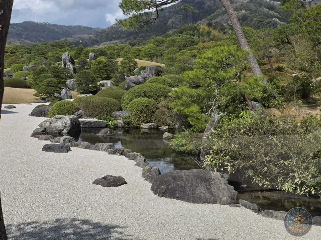 Landscape view of pristine white gravel raked paths, serene pond, sculpted pine trees, and lush green mountain backdrop at the Adachi Museum of Art during a cruise port visit at Sakaiminato Japan Cruise Port Guide, DIY Sakaiminato Cruise Port to City Center, Things to do in Sakaiminato from cruise ship, Westerdam Sakaiminato Docking Location, One day in Sakaiminato Japan itinerary by Danny and Peter.