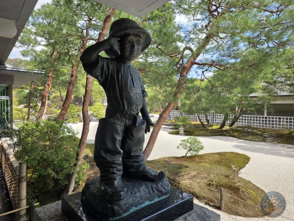 Bronze statue of a young boy wearing a hat and oversized boots overlooking the pine trees and raked sand of the Japanese garden at the Adachi Museum of Art during a shore excursion from Sakaiminato Japan Cruise Port Guide, DIY Sakaiminato Cruise Port to City Center, Things to do in Sakaiminato from cruise ship, Westerdam Sakaiminato Docking Location, One day in Sakaiminato Japan itinerary by Danny and Peter.