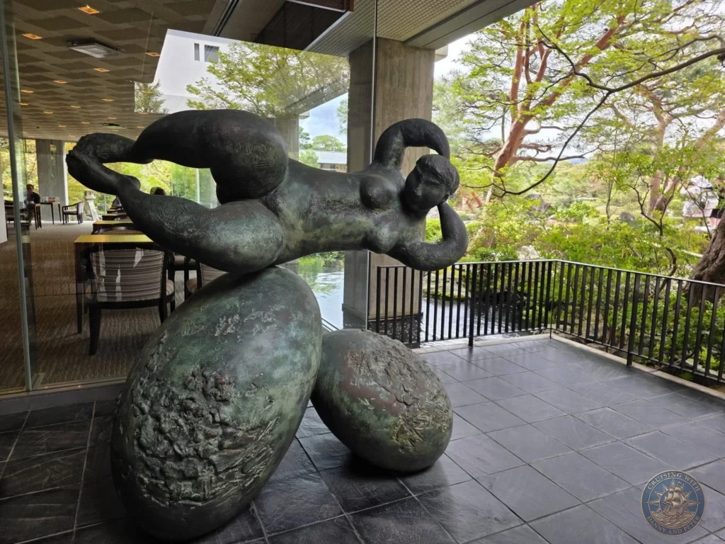 Bronze reclining figure sculpture balanced atop large stones inside a glass atrium overlooking Japanese garden greenery at the Adachi Museum of Art during a shore excursion from Sakaiminato Japan Cruise Port Guide, DIY Sakaiminato Cruise Port to City Center, Things to do in Sakaiminato from cruise ship, Westerdam Sakaiminato Docking Location, One day in Sakaiminato Japan itinerary by Danny and Peter.