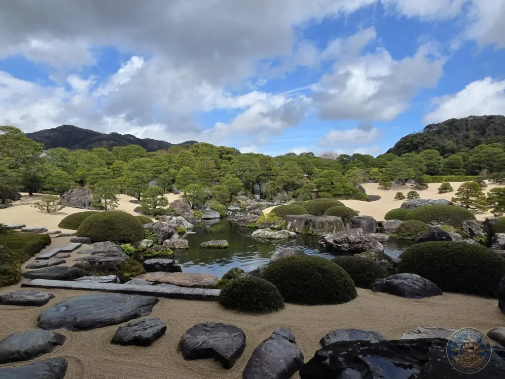 Panoramic view of the manicured dry landscape garden, central pond, manicured pine trees, and distant mountains under a blue sky at the Adachi Museum of Art during a shore excursion from Sakaiminato Japan Cruise Port Guide, DIY Sakaiminato Cruise Port to City Center, Things to do in Sakaiminato from cruise ship, Westerdam Sakaiminato Docking Location, One day in Sakaiminato Japan itinerary by Danny and Peter.