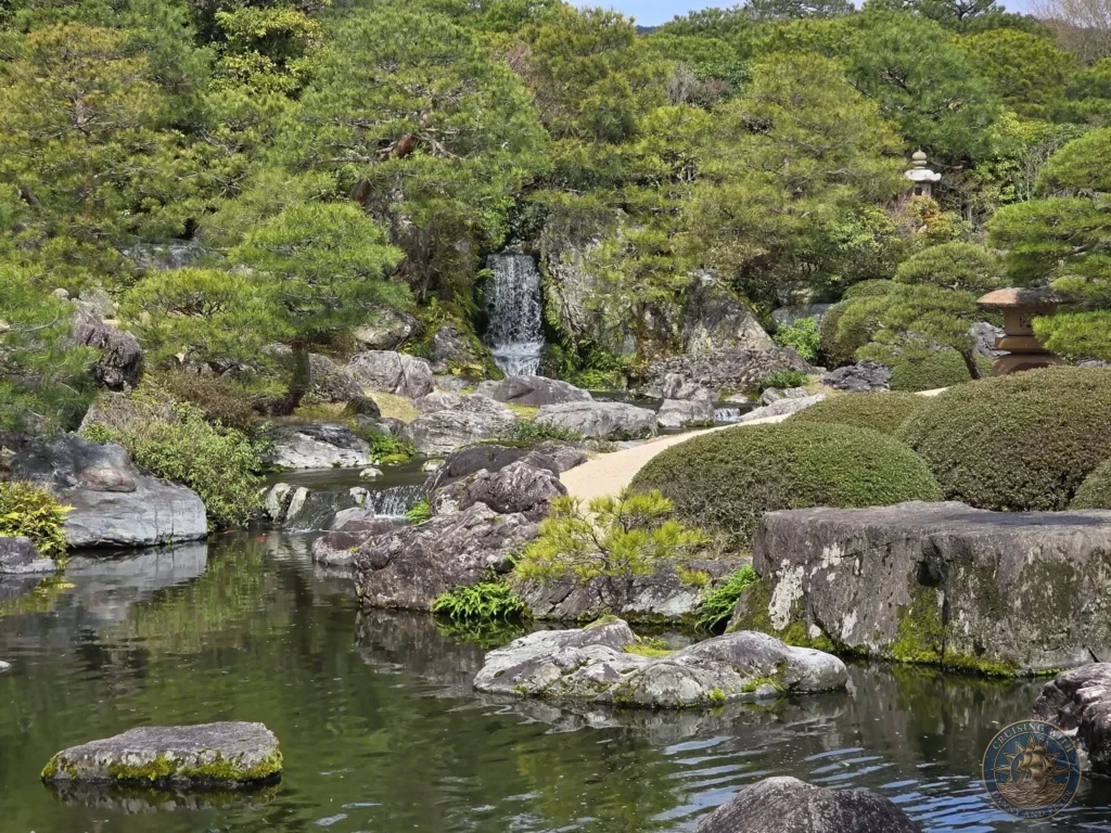 Picturesque garden waterfall cascading down rocky cliffs into a tranquil pond surrounded by manicured pine trees and stone lanterns at the Adachi Museum of Art during a shore excursion from Sakaiminato Japan Cruise Port Guide, DIY Sakaiminato Cruise Port to City Center, Things to do in Sakaiminato from cruise ship, Westerdam Sakaiminato Docking Location, One day in Sakaiminato Japan itinerary by Danny and Peter.