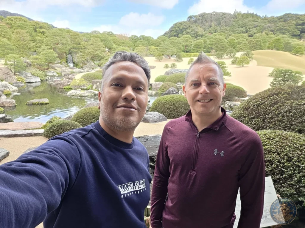 Danny and Peter taking a selfie together in front of the manicured dry landscape gardens, pond, and waterfall at the Adachi Museum of Art during a shore excursion from Sakaiminato Japan Cruise Port Guide, DIY Sakaiminato Cruise Port to City Center, Things to do in Sakaiminato from cruise ship, Westerdam Sakaiminato Docking Location, One day in Sakaiminato Japan itinerary by Danny and Peter.