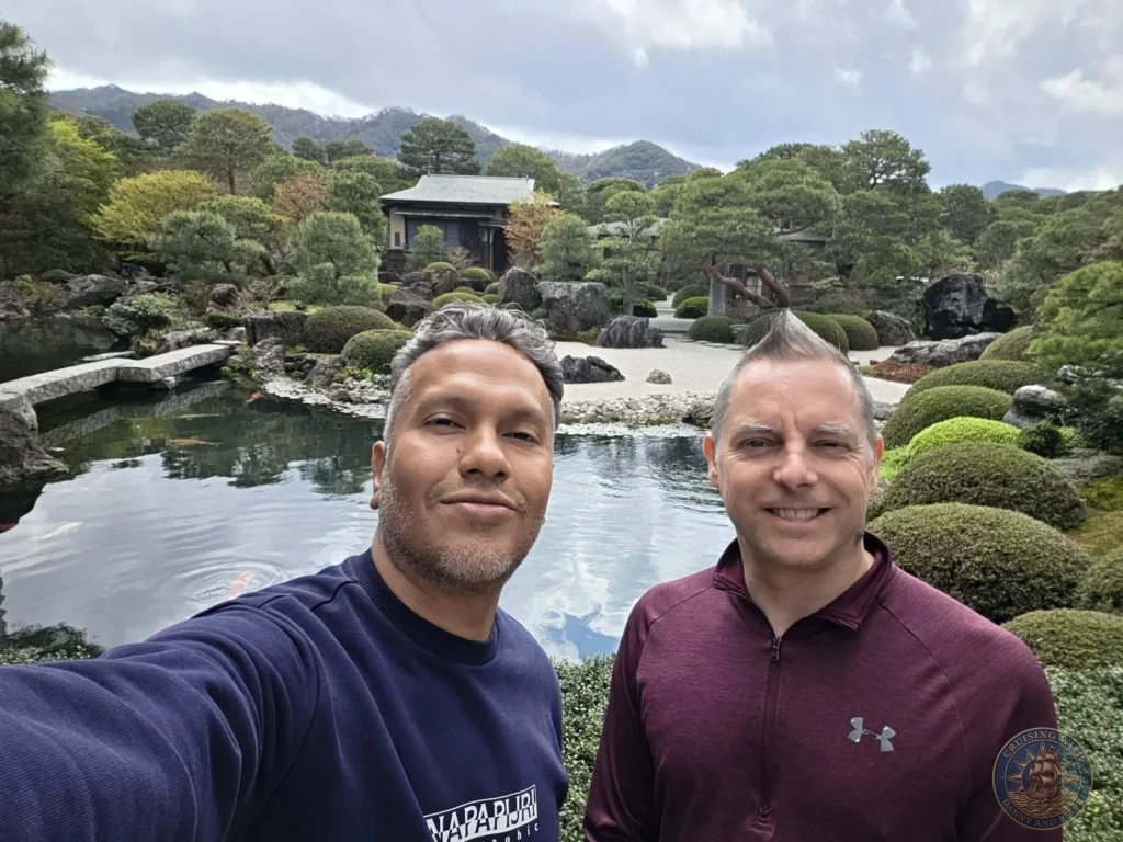 Danny and Peter smiling together in a selfie in front of the koi pond, stone bridge, and tea house at the Adachi Museum of Art during a shore excursion from Sakaiminato Japan Cruise Port Guide, DIY Sakaiminato Cruise Port to City Center, Things to do in Sakaiminato from cruise ship, Westerdam Sakaiminato Docking Location, One day in Sakaiminato Japan itinerary by Danny and Peter.