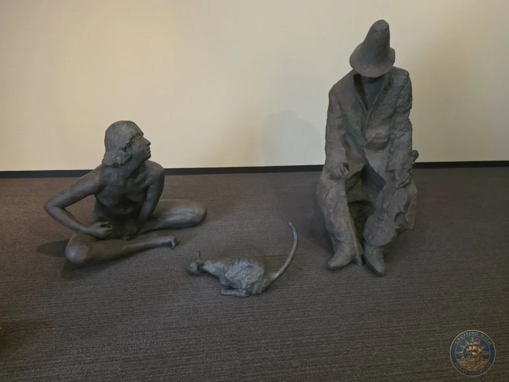 Bronze sculptures of a seated violinist wearing a hat, a reclining figure looking upward, and a cat on carpeted display floor inside the Adachi Museum of Art gallery during a shore excursion from Sakaiminato Japan Cruise Port Guide, DIY Sakaiminato Cruise Port to City Center, Things to do in Sakaiminato from cruise ship, Westerdam Sakaiminato Docking Location, One day in Sakaiminato Japan itinerary by Danny and Peter.