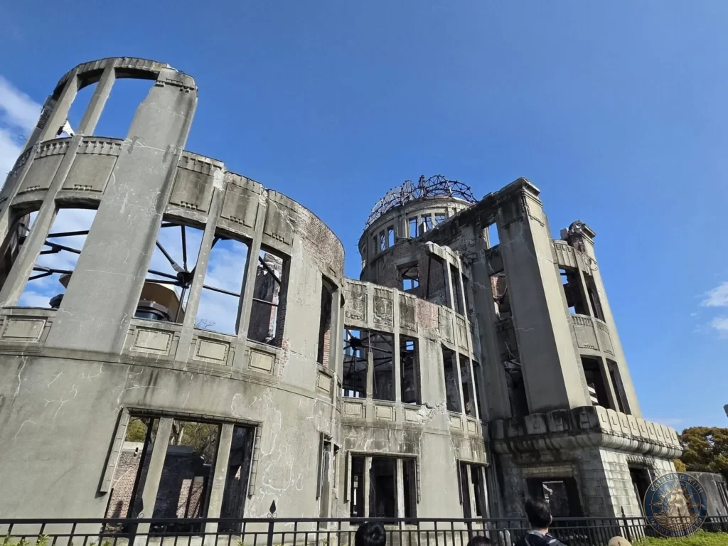 Hiroshima Japan Cruise Port Guide 2026 – Insider Tips & One Day Itinerary 22 Low-angle close-up view looking up at the preserved concrete façade and exposed copper dome skeleton of the Atomic Bomb Dome against a blue sky in Hiroshima. Hiroshima Japan Cruise Port Guide, DIY Hiroshima Cruise Port to City Center, Things to do in Hiroshima from cruise ship, Westerdam Hiroshima Docking Location, One day in Hiroshima Japan itinerary by Danny and Peter.