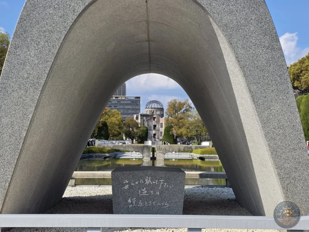 Hiroshima Japan Cruise Port Guide 2026 – Insider Tips & One Day Itinerary 59 Close up view looking through the concrete arch of the Memorial Cenotaph for A-Bomb Victims, showing the engraved epitaph stone and framing the distant Atomic Bomb Dome in Hiroshima Peace Memorial Park Japan. Hiroshima Japan Cruise Port Guide, DIY Hiroshima Cruise Port to City Center, Things to do in Hiroshima from cruise ship, Westerdam Hiroshima Docking Location, One day in Hiroshima Japan itinerary by Danny and Peter.