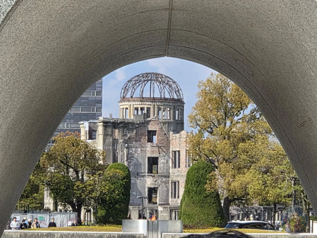 Hiroshima Japan Cruise Port Guide 2026 – Insider Tips & One Day Itinerary 60 Framed view looking through the concrete arch of the Memorial Cenotaph toward the Flame of Peace and the historic Atomic Bomb Dome in Hiroshima Peace Memorial Park Japan. Hiroshima Japan Cruise Port Guide, DIY Hiroshima Cruise Port to City Center, Things to do in Hiroshima from cruise ship, Westerdam Hiroshima Docking Location, One day in Hiroshima Japan itinerary by Danny and Peter.