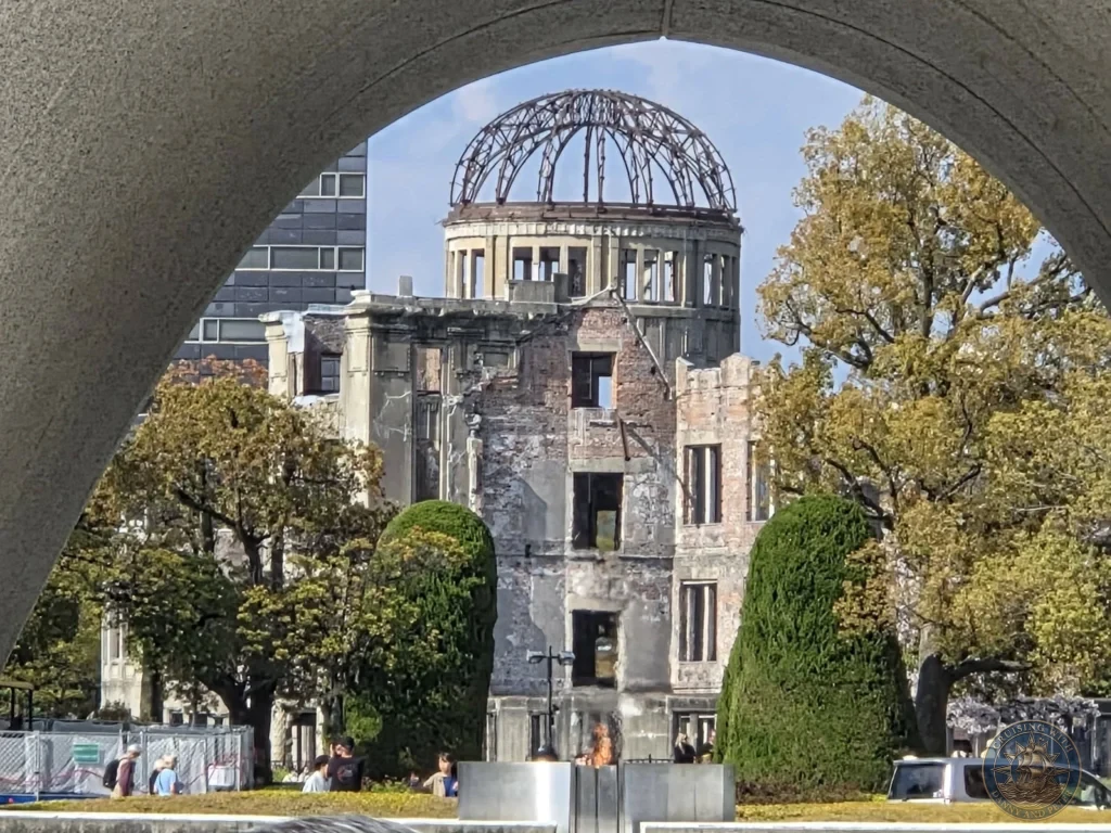 Hiroshima Japan Cruise Port Guide 2026 – Insider Tips & One Day Itinerary 61 Close up framed shot looking directly through the Memorial Cenotaph arch toward the steel framework of the Atomic Bomb Dome in Hiroshima Peace Memorial Park Japan. Hiroshima Japan Cruise Port Guide, DIY Hiroshima Cruise Port to City Center, Things to do in Hiroshima from cruise ship, Westerdam Hiroshima Docking Location, One day in Hiroshima Japan itinerary by Danny and Peter.
