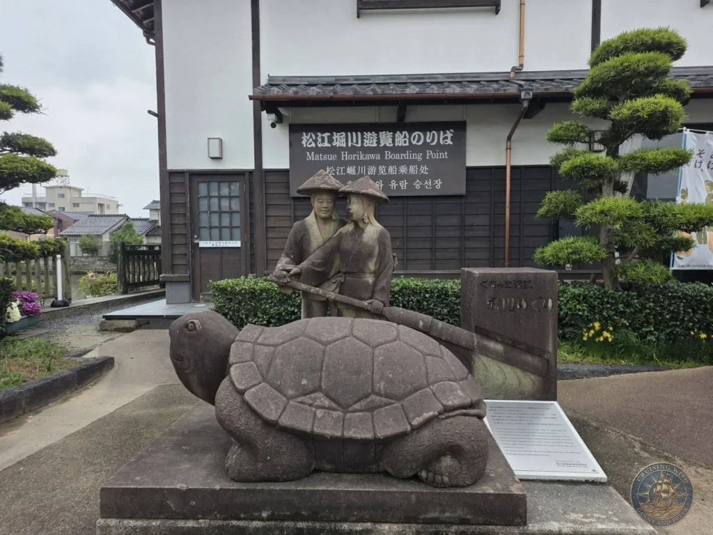 Stone turtle sculpture and boatmen statues standing outside the Matsue Horikawa Sightseeing Boat Boarding Point entrance building during a shore excursion from Sakaiminato Japan Cruise Port Guide, DIY Sakaiminato Cruise Port to City Center, Things to do in Sakaiminato from cruise ship, Westerdam Sakaiminato Docking Location, One day in Sakaiminato Japan itinerary by Danny and Peter.