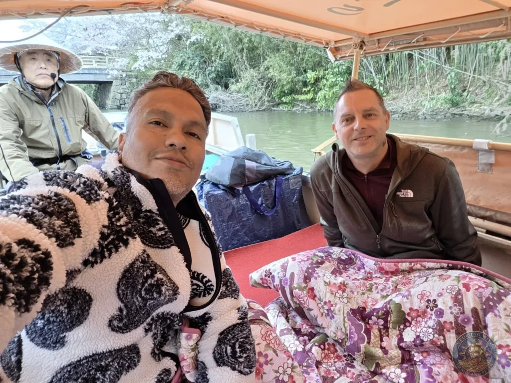 Selfie on board a traditional Horikawa Sightseeing Boat under a covered canopy with a boat captain steering in the background along the Matsue castle moat during a shore excursion from Sakaiminato Japan Cruise Port Guide, DIY Sakaiminato Cruise Port to City Center, Things to do in Sakaiminato from cruise ship, Westerdam Sakaiminato Docking Location, One day in Sakaiminato Japan itinerary by Danny and Peter.