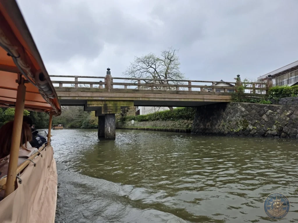 View from a low-slung sightseeing boat approaching a traditional wooden bridge spanning the water along the Matsue Castle moat during a shore excursion from Sakaiminato Japan Cruise Port Guide, DIY Sakaiminato Cruise Port to City Center, Things to do in Sakaiminato from cruise ship, Westerdam Sakaiminato Docking Location, One day in Sakaiminato Japan itinerary by Danny and Peter.