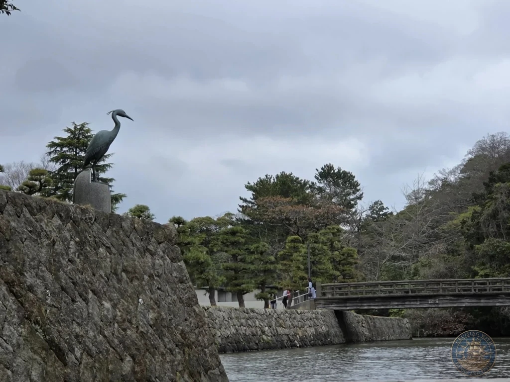 Bronze heron bird statue mounted atop the historic stone moat wall along the Horikawa Canal near Matsue Castle during a shore excursion from Sakaiminato Japan Cruise Port Guide, DIY Sakaiminato Cruise Port to City Center, Things to do in Sakaiminato from cruise ship, Westerdam Sakaiminato Docking Location, One day in Sakaiminato Japan itinerary by Danny and Peter.