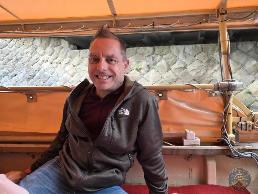Peter seated inside the orange-canopied Horikawa Sightseeing Boat in front of historic stone moat walls in Matsue during a shore excursion from Sakaiminato Japan Cruise Port Guide, DIY Sakaiminato Cruise Port to City Center, Things to do in Sakaiminato from cruise ship, Westerdam Sakaiminato Docking Location, One day in Sakaiminato Japan itinerary by Danny and Peter.