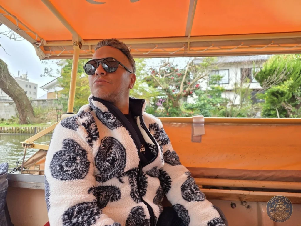 Danny wearing sunglasses and a patterned fleece jacket looking out from beneath the orange canopy of the Horikawa Sightseeing Boat in Matsue during a shore excursion from Sakaiminato Japan Cruise Port Guide, DIY Sakaiminato Cruise Port to City Center, Things to do in Sakaiminato from cruise ship, Westerdam Sakaiminato Docking Location, One day in Sakaiminato Japan itinerary by Danny and Peter.