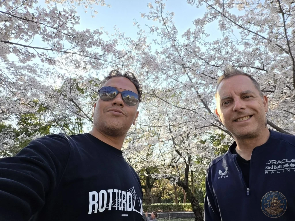 Hiroshima Japan Cruise Port Guide 2026 – Insider Tips & One Day Itinerary 35 Selfie under a full canopy of blooming cherry blossom trees on a bright day in Hiroshima Japan. Hiroshima Japan Cruise Port Guide, DIY Hiroshima Cruise Port to City Center, Things to do in Hiroshima from cruise ship, Westerdam Hiroshima Docking Location, One day in Hiroshima Japan itinerary by Danny and Peter.