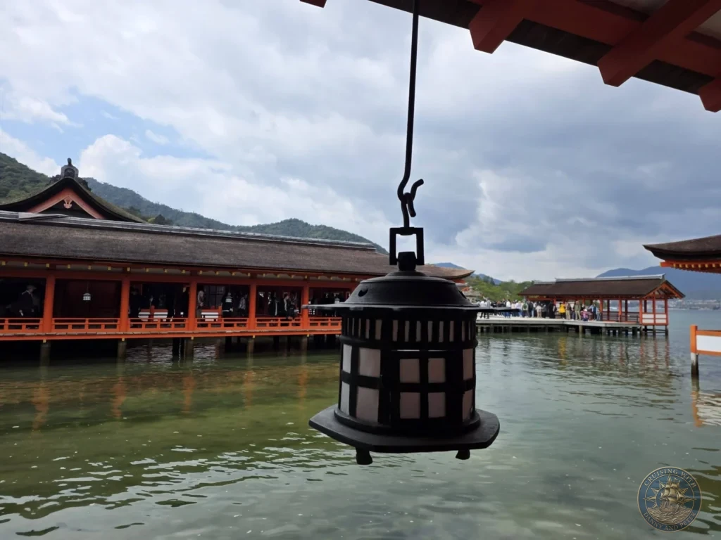 Hiroshima Japan Cruise Port Guide 2026 – Insider Tips & One Day Itinerary 11 Close-up of a bronze hanging lantern suspended from the orange wooden corridors over the water at Itsukushima Shrine on Miyajima Island in Hiroshima Japan. Hiroshima Japan Cruise Port Guide, DIY Hiroshima Cruise Port to City Center, Things to do in Hiroshima from cruise ship, Westerdam Hiroshima Docking Location, One day in Hiroshima Japan itinerary by Danny and Peter.