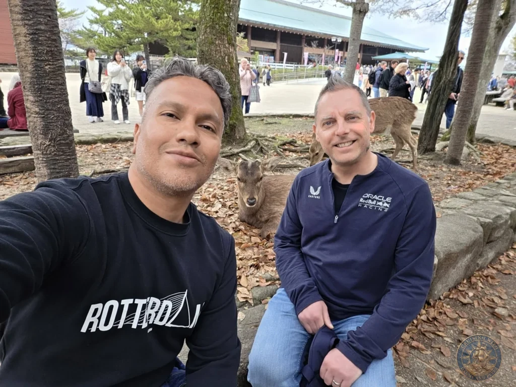 Hiroshima Japan Cruise Port Guide 2026 – Insider Tips & One Day Itinerary 27 Danny and Peter smiling while sitting near wild sika deer resting under trees on Miyajima Island in Hiroshima Japan. Hiroshima Japan Cruise Port Guide, DIY Hiroshima Cruise Port to City Center, Things to do in Hiroshima from cruise ship, Westerdam Hiroshima Docking Location, One day in Hiroshima Japan itinerary by Danny and Peter.