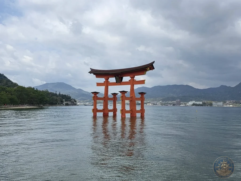 Hiroshima Japan Cruise Port Guide 2026 – Insider Tips & One Day Itinerary 30 Symmetrical wide shot of the grand vermilion floating Torii Gate of Itsukushima Shrine reflecting in the water at high tide with distant mountains on Miyajima Island in Hiroshima Japan. Hiroshima Japan Cruise Port Guide, DIY Hiroshima Cruise Port to City Center, Things to do in Hiroshima from cruise ship, Westerdam Hiroshima Docking Location, One day in Hiroshima Japan itinerary by Danny and Peter.