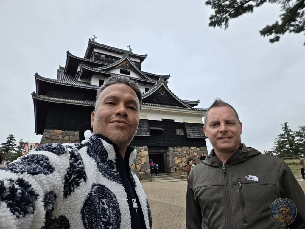 Danny and Peter taking a close-up selfie in front of the iconic black wooden keep and stone wall base of Matsue Castle during a shore excursion from Sakaiminato Japan Cruise Port Guide, DIY Sakaiminato Cruise Port to City Center, Things to do in Sakaiminato from cruise ship, Westerdam Sakaiminato Docking Location, One day in Sakaiminato Japan itinerary by Danny and Peter.