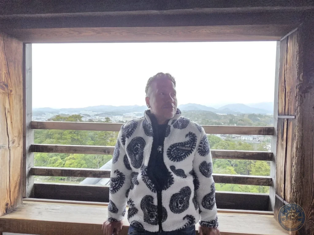 Danny posing inside the upper floor of Matsue Castle framed by a large historic wooden window overlooking treetops and distant mountains during a shore excursion from Sakaiminato Japan Cruise Port Guide, DIY Sakaiminato Cruise Port to City Center, Things to do in Sakaiminato from cruise ship, Westerdam Sakaiminato Docking Location, One day in Sakaiminato Japan itinerary by Danny and Peter.